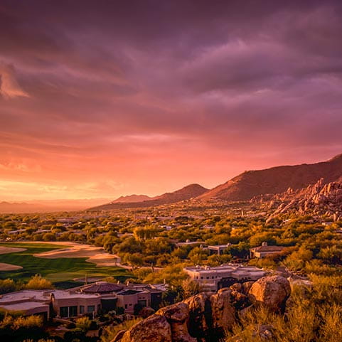 A scenic sunset view of a golf course in Scottsdale, Arizona, with mountains in the background.