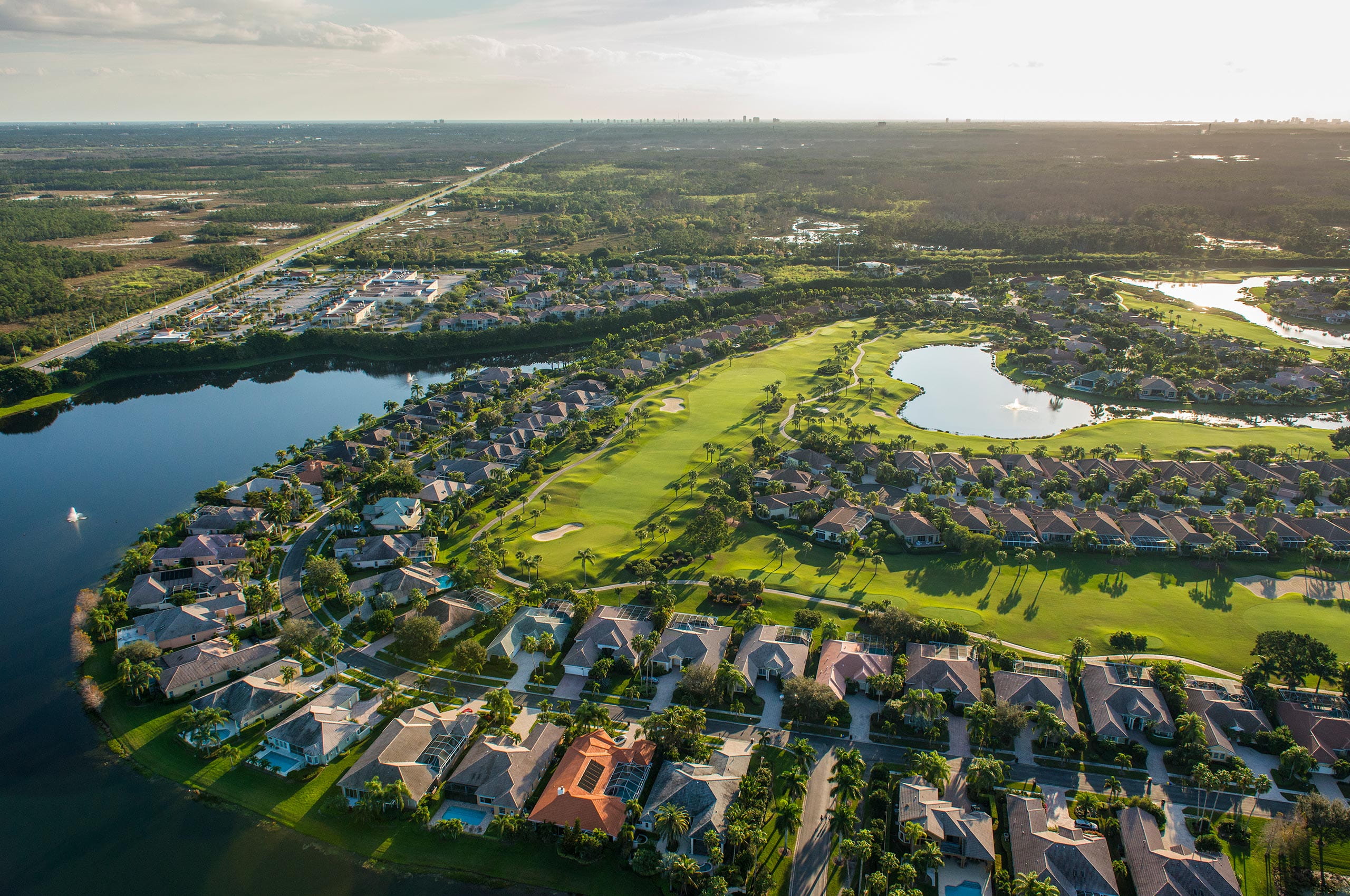 Aerial view of golf course with houses, trees, and roads in a residential area.